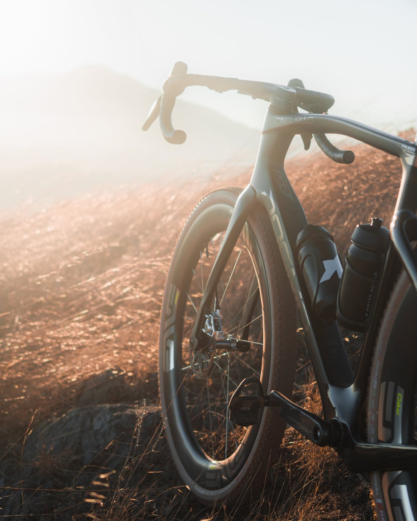 Pinarello Dogma GR from the side, handlebars and rear wheel lit by low sun on a dry hillside